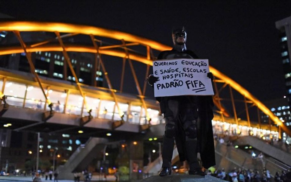 Protestujący w stroju Batmana przed stadionem w Rio. Na kartce napis: "Chcemy edukacji, zdrowia, szk