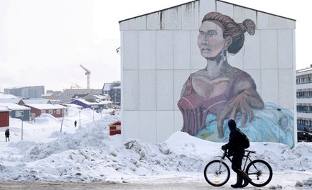 Mężczyzna mija budynek socjalny z muralem w języku inuickim w Nuuk na Grenlandii