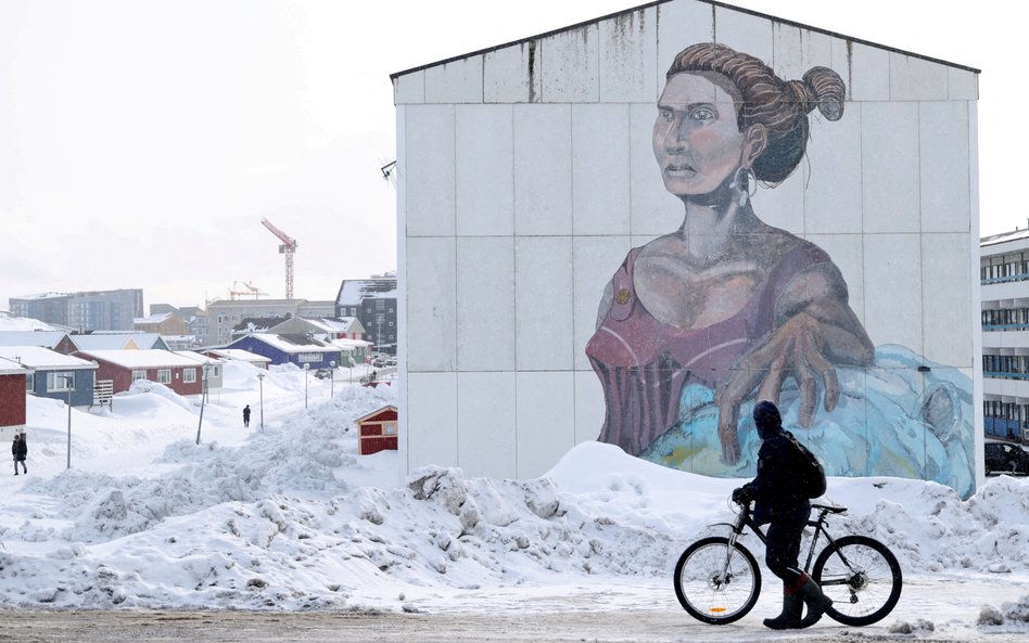Mężczyzna mija budynek socjalny z muralem w języku inuickim w Nuuk na Grenlandii