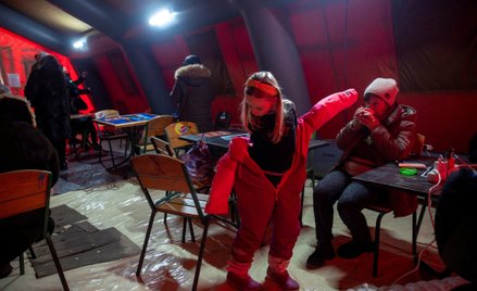 Ludzie ogrzewają się w namiocie udostępnionym przez służby ratunkowe mieszkańcom Kijowa, których mie