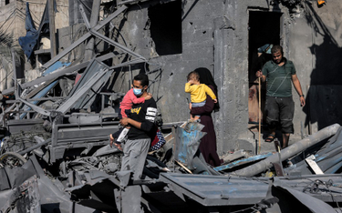 Mężczyzna i kobieta idą niosą dzieci obok gruzów budynku zniszczonego przez Izrael w Rafah w południ