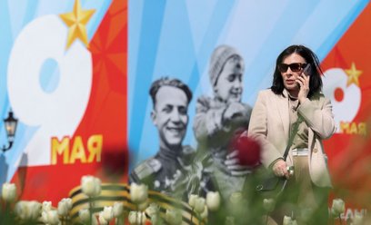Kobieta rozmawia przez telefon przed banerem reklamującym paradę wojskową z okazji Dnia Zwycięstwa. 