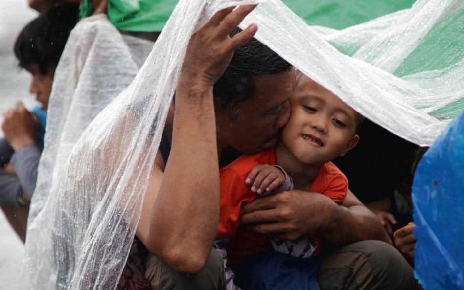 Filipińczyk, który ocalał z tajfunu, czeka z synem na ewakuację na lotnisku polowym Tacloban. Oni i 