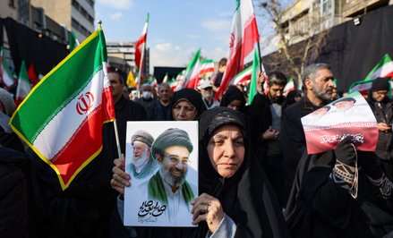 Proreżimowa demonstrantka w Iranie trzyma w ręku grafikę przedstawiającą na pierwszym planie Modżtab