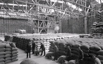 Wnętrze hali w łuszczarni ryżu (widoczne worki z ryżem oraz robotnicy przewożący worki na wózkach). 