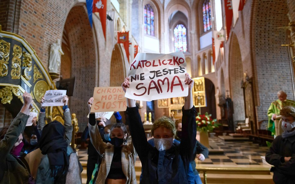 Grupa osób stanęła przed ołtarzem z transparentami o treściach związanych z prawem do aborcji; msza 