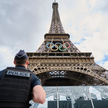 Policjant  przed Wieżą Eiffla w Paryżu, ozdobioną symbolem Igrzysk Olimpijskich