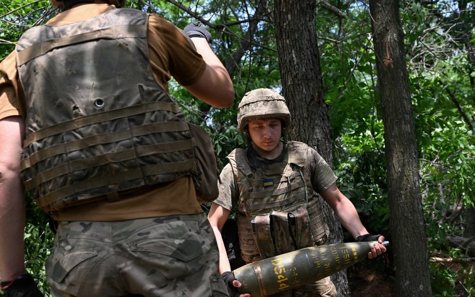 Ukraiński artylerzysta przenosi pocisk 155 mm, aby wystrzelić haubicę M777 w kierunku rosyjskich poz