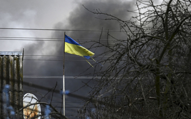 Flaga Ukrainy na tle dymu unoszącego się ze zbombardowanego magazynu w miejscowości Stojanka na zach