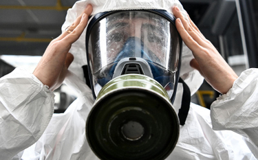 Pracownik Ministerstwa Sytuacji Nadzwyczajnych ubrany w sprzęt ochronny poprawia maskę podczas dezyn