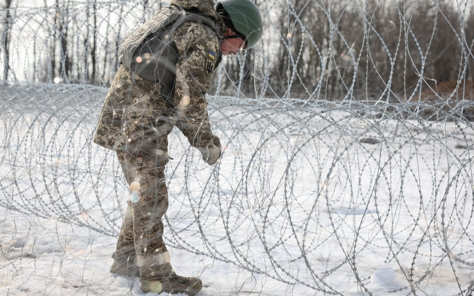 Ukraiński żołnierz instaluje drut kolczasty w pobliżu linii frontu na przedmieściach Kupiańska