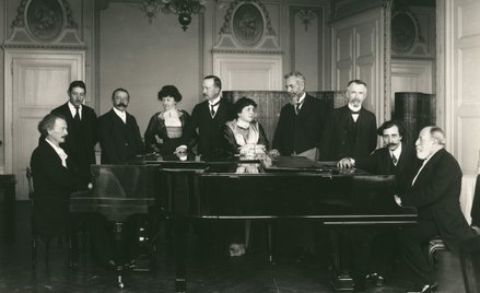 Ignacy Jan Paderewski i Camille Saint-Saëns przy fortepianach. Wśród gości w środku żona, Helena Pad