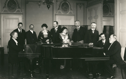 Ignacy Jan Paderewski i Camille Saint-Saëns przy fortepianach. Wśród gości w środku żona, Helena Pad