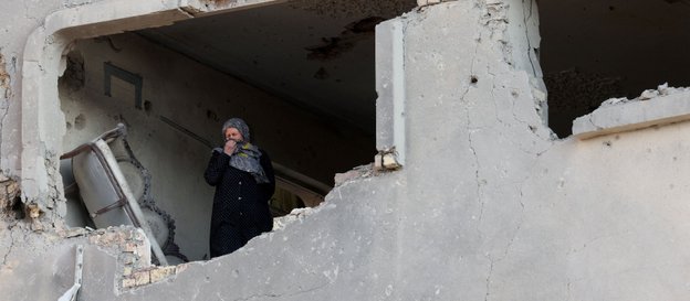 Kobieta wygląda z okna budynku, który ucierpiał w nalocie na Teheran