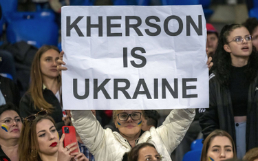 Kobieta trzyma plakat z napisem "Chersoń jest Ukrainą" podczas charytatywnego meczu piłkarskiego Mat