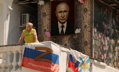 Kobieta spogląda z balkonu ozdobionego flagami rosyjskiej marynarki wojennej i symbolami narodowymi 