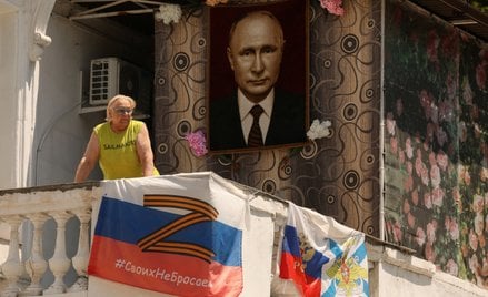 Kobieta spogląda z balkonu ozdobionego flagami rosyjskiej marynarki wojennej i symbolami narodowymi 