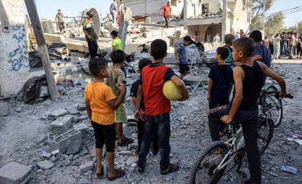 Dzieci obserwują, jak ratownicy szukają ofiar w gruzach budynku po izraelskim nalocie w Rafah w połu