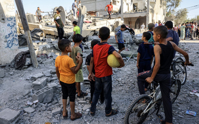 Dzieci obserwują, jak ratownicy szukają ofiar w gruzach budynku po izraelskim nalocie w Rafah w połu