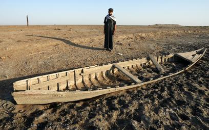 Iracki rybak obok swej łodzi na wyschniętych mokradłach Al-Chibayish in południowym Iraku.
