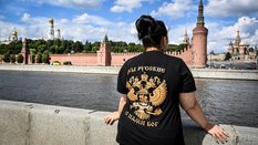 Kobieta ubrana w koszulkę z godłem państwowym Rosji i napisem „Jesteśmy Rosjanami, Bóg z nami” stoi 