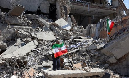 Mężczyzna trzyma irańską flagę wśród gruzów zniszczonego budynku po nalotach w centrum Teheranu