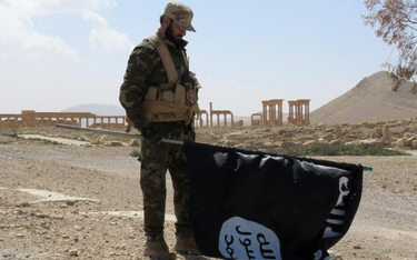 Żołnierz sił rządowych ze zdobytą flagą tzw. Państwa Islamskiego w odbitej z rąk dżihadystów Palmirz
