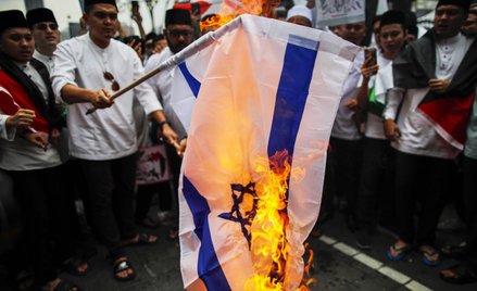 Protestujący palą izraelską flagę narodową podczas solidarności z Palestyńczykami po nalocie policji