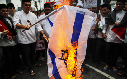 Protestujący palą izraelską flagę narodową podczas solidarności z Palestyńczykami po nalocie policji