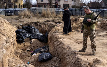 Żołnierze nad masowym grobem w Buczy