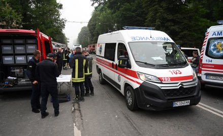 Ratownicy stoją w pobliżu budynku mieszkalnego, częściowo zniszczonego przez uderzenie rakietowe we 