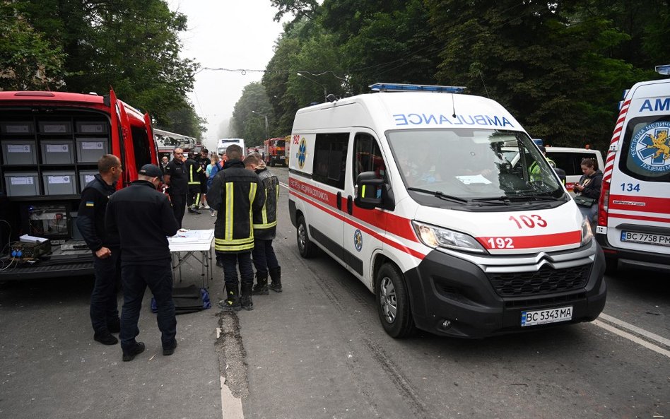 Ratownicy stoją w pobliżu budynku mieszkalnego, częściowo zniszczonego przez uderzenie rakietowe we 