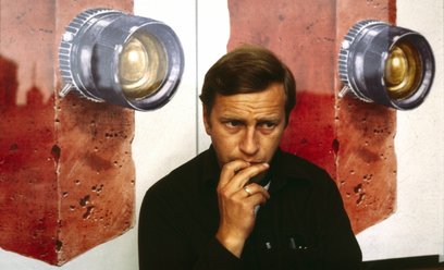 Jerzy Stuhr, odtwórca roli Filipa Mosza, na tle plakatu autorstwa Andrzeja Pągowskiego do filmu „Ama