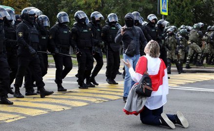 Białorusinka klęczy przed funkcjonariuszami OMON podczas wiecu w Mińsku, 13 września