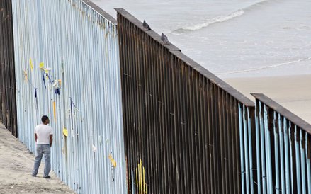 Mężczyzna przygląda się dziurze w ogrodzeniu zbudowanym wzdłuż granicy amerykańsko-meksykańskiej w T