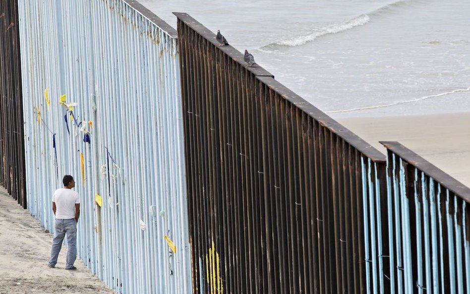 Mężczyzna przygląda się dziurze w ogrodzeniu zbudowanym wzdłuż granicy amerykańsko-meksykańskiej w T