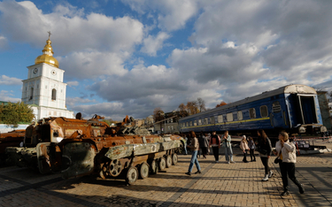Ludzie mijają uszkodzony wagon kolejowy i zniszczone rosyjskie maszyny wojskowe wystawione w pobliżu