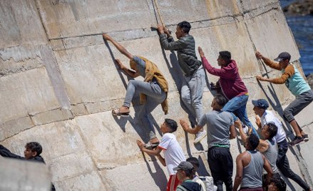 Migranci wspinają się na wał morski w marokańskim mieście Fnideq po nieudanej próbie przekroczenia g