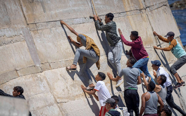 Migranci wspinają się na wał morski w marokańskim mieście Fnideq po nieudanej próbie przekroczenia g