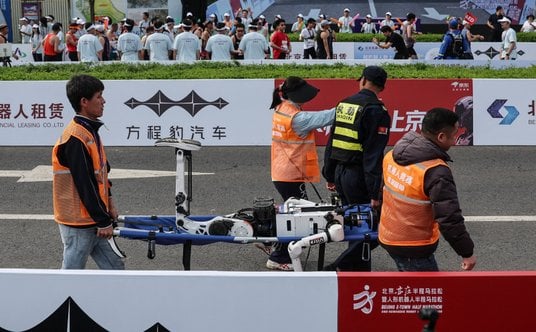 Pracownicy niosą humanoidalnego robota, który rozbił się po przekroczeniu linii mety półmaratonu w P