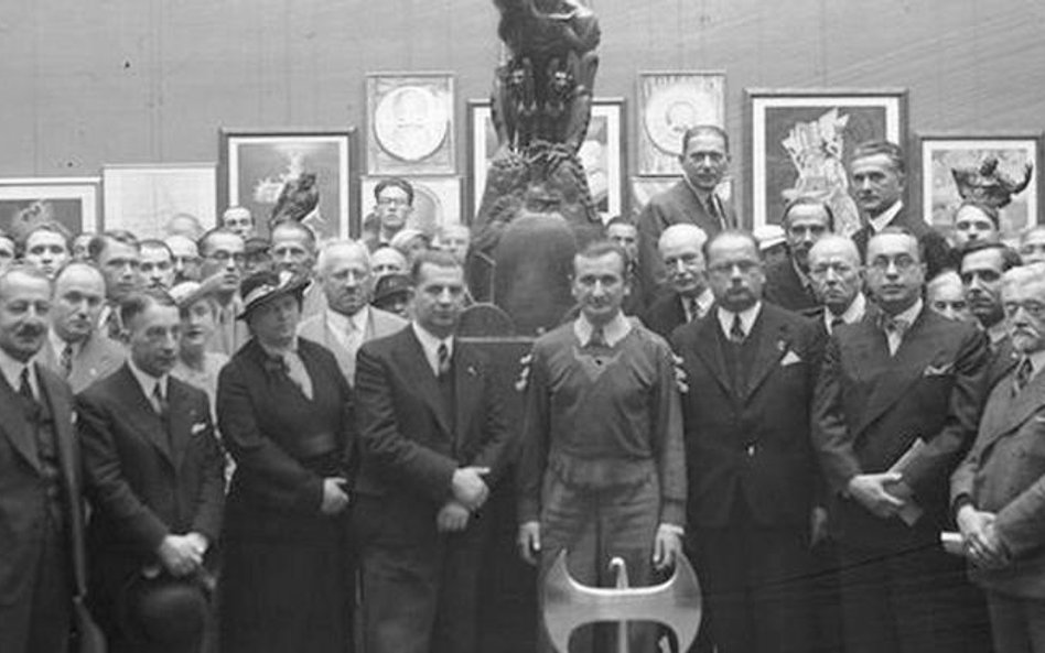 Stanisław Szukalski na wernisażu wystawy w Krakowie w 1936 r. Stoi w środku, przed nim toporzeł jego