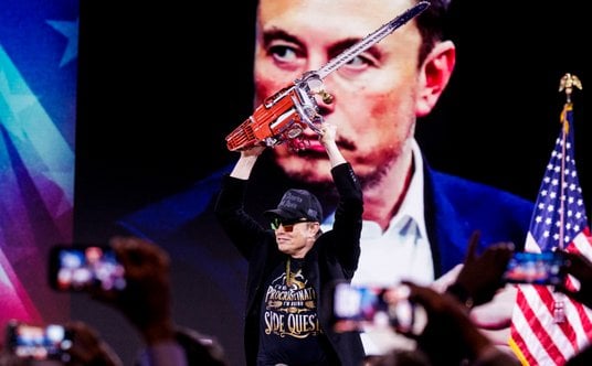 Elon Musk trzyma piłę łańcuchową podarowaną mu przez Javiera Milei, prezydenta Argentyny, podczas ko