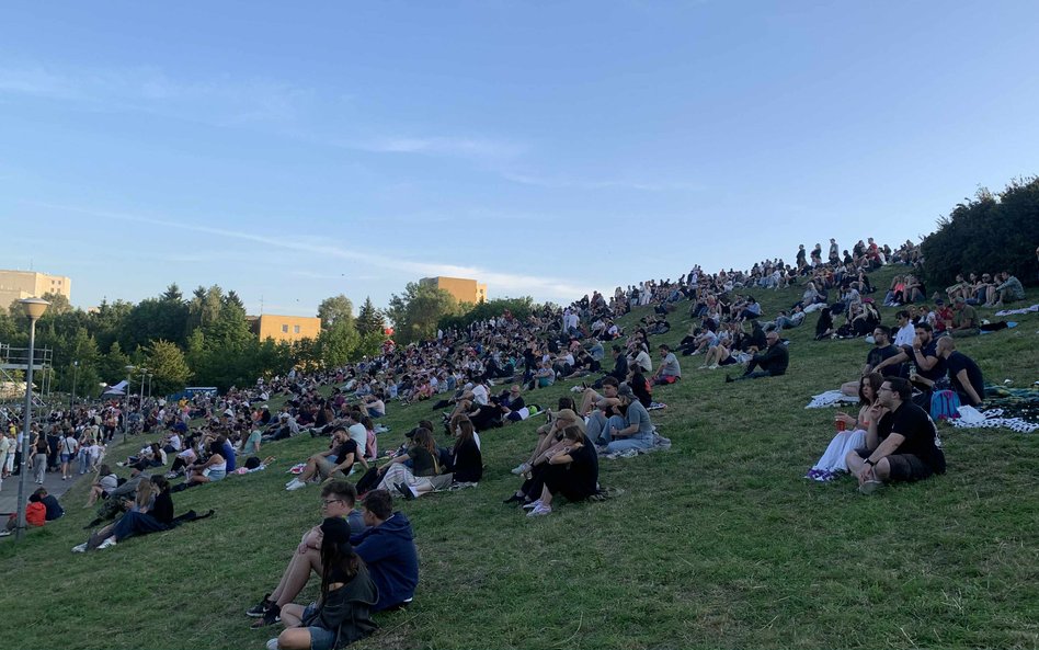 Uczestnicy festiwalu odpoczywają na trawie, rozmawiając i słuchając muzyki