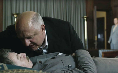 Ławrentij Beria (Simon Russell Beale) pochyla się nad martwym wodzem (Gary Oldman) – scena z filmu.