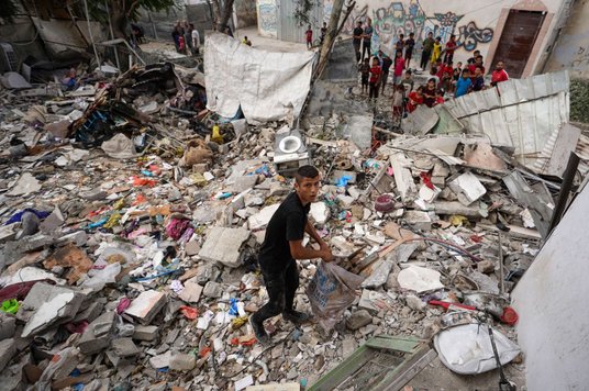 Młody Palestyńczyk zbiera przedmioty w ruinach domu zbombardowanego przez wojsko Izraela, Nusajrat w