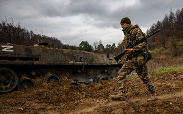 Ukraiński żołnierz obok zniszczonego rosyjskiego transportera piechoty