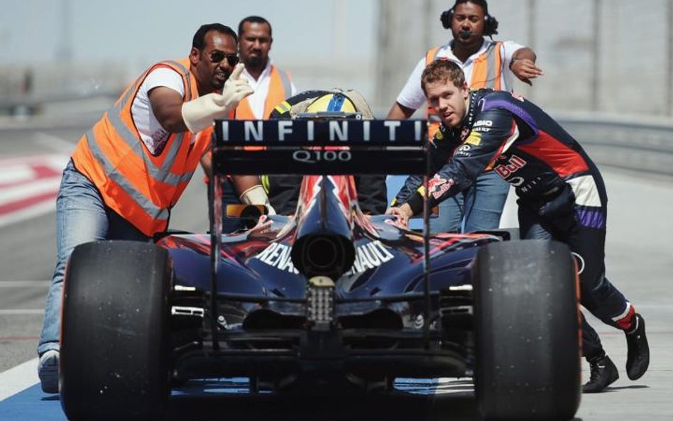 Mistrz świata Sebastian Vettel (pierwszy z prawej) pcha w Bahrajnie swój popsuty samochód do garażu