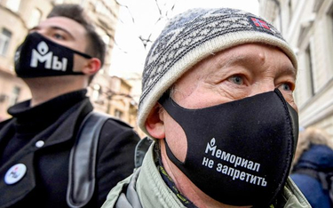 Demonstranci przed gmachem w maskach ze słynnym logo Memoriału