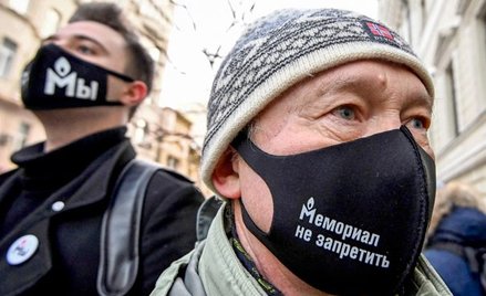 Demonstranci przed gmachem w maskach ze słynnym logo Memoriału