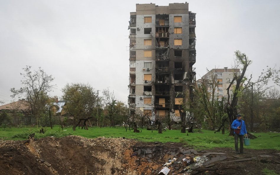Mężczyzna stoi obok krateru powstałego po rosyjskim uderzeniu wojskowym – w czasie rosyjskiego ataku